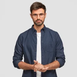 waist-up-portrait-handsome-serious-unshaven-male-keeps-hands-together-dressed-dark-blue-shirt-has-talk-with-interlocutor-stands-against-white-wall-self-confident-man-freelancer